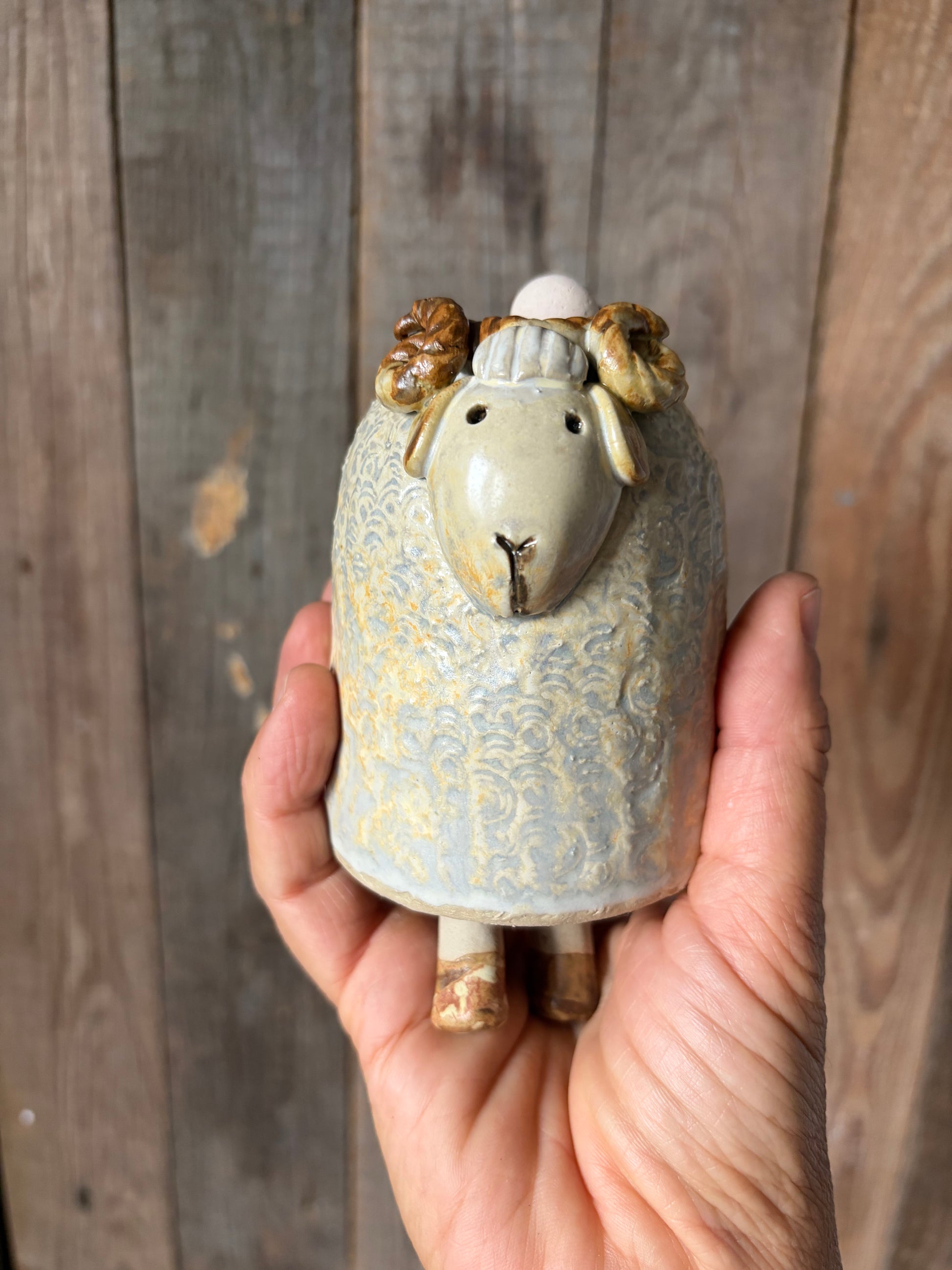 una mano regge una tintinnante campanella in gres a forma di montone