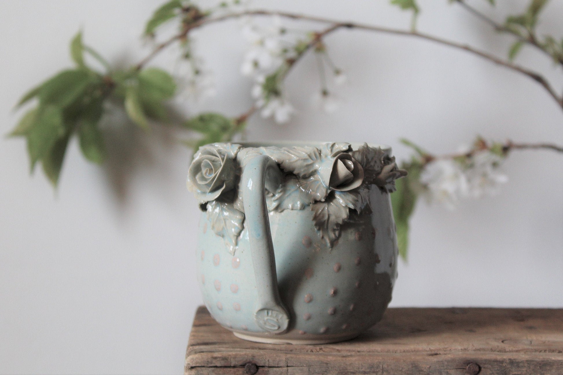 Tazza Alice in gres azzurro con rose bianche e puntini rosa in rilievo, fatta a mano al tornio