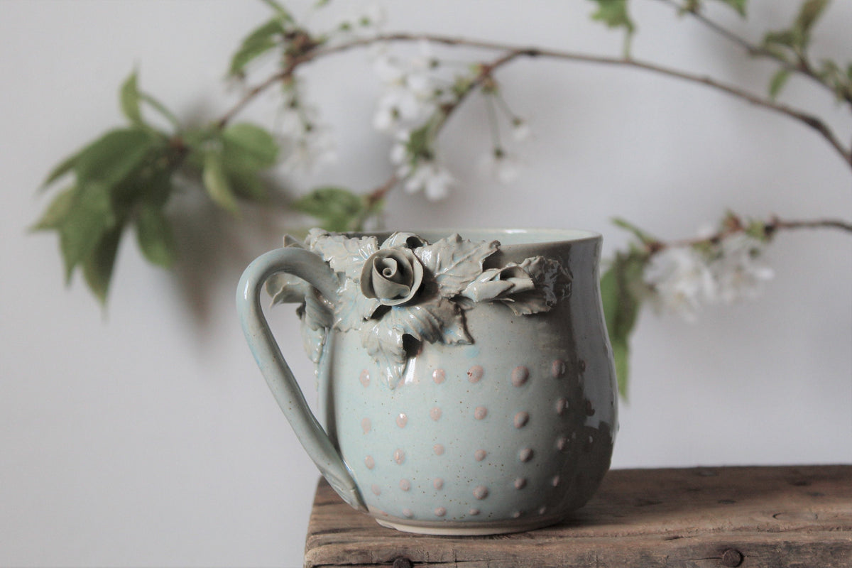 Tazza Alice in gres azzurro con rose bianche e puntini rosa in rilievo, fatta a mano al tornio